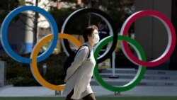 Женщина в маске проходит в Токио рядом с инсталляцией в форме олимпийских колец.