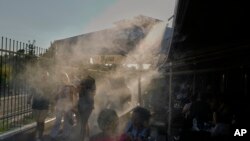 Людзі, каб астудзіцца, праходзяць праз апарат, якія распыляе вільгаць. Атэны, Грэцыя, 1 ліпеня 2025 году