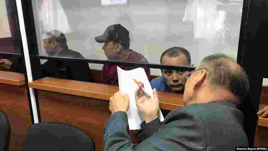 Өртенген автобус ісі бойынша күдікті деп танылған жүргізушілер (әйнек камера ішінде солдан оңға қарай) - Барат Таңатов, Нұржан Қырғызбаев, Мақсат Пернебеков сотта адвокат Хайрулла Әлимағамбетовпен сөйлесіп отыр. Айыпталушылар бес жылға сотталды. Ақтөбе. 3 қыркүйек 2018 жыл. &nbsp;